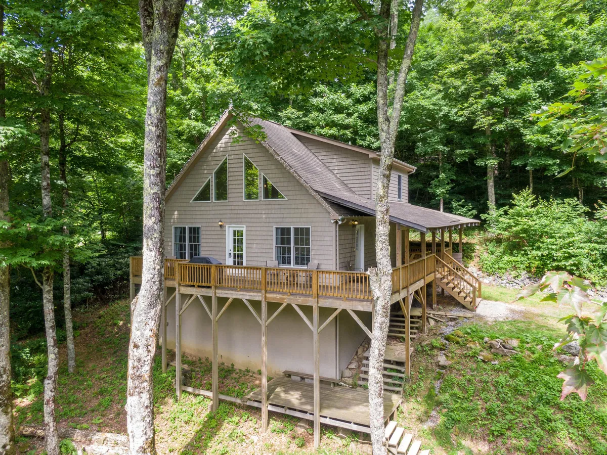 This image showcases a spacious wooden deck with large windows, enveloped by lush natural surroundings. The setting sun adds warmth and ambiance, while the deck appears ideal for outdoor relaxation, morning coffee, and evening star-gazing.