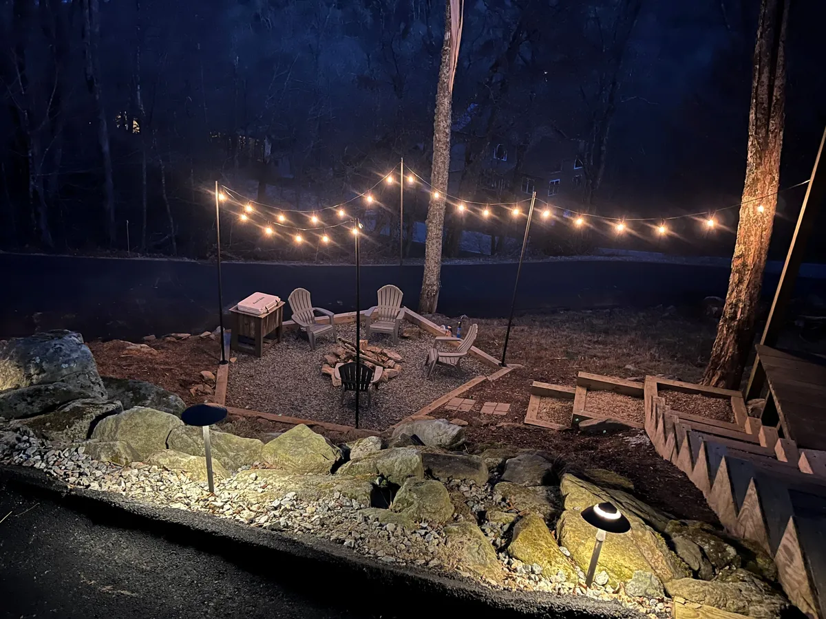 A charming fire pit area with adirondack chairs and string lights, nestled among trees. The inviting setup suggests a perfect spot for gathering, storytelling, and enjoying evenings under the stars.