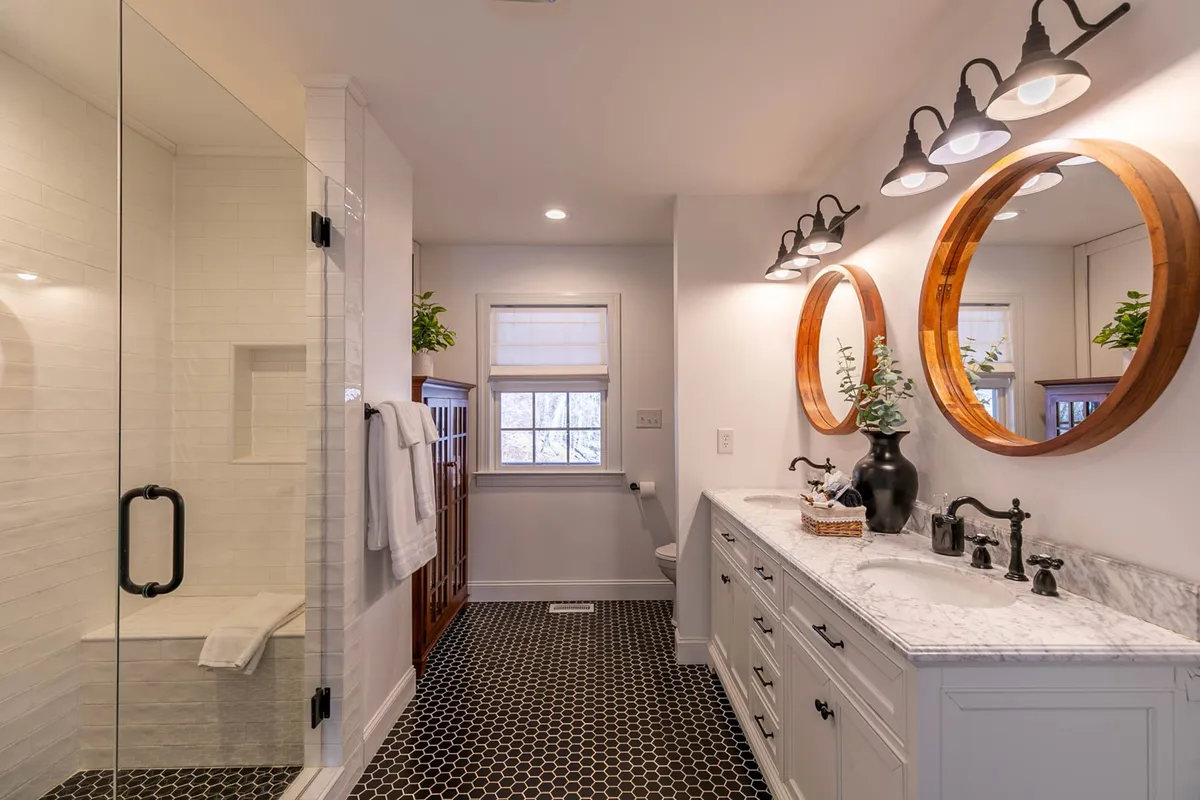 A modern bathroom with double mirror sinks, sleek light fixtures, striking black and white tile flooring, and a glass-enclosed shower area. The design is contemporary and functional, providing a spacious and luxurious atmosphere for self-care routines and relaxation.