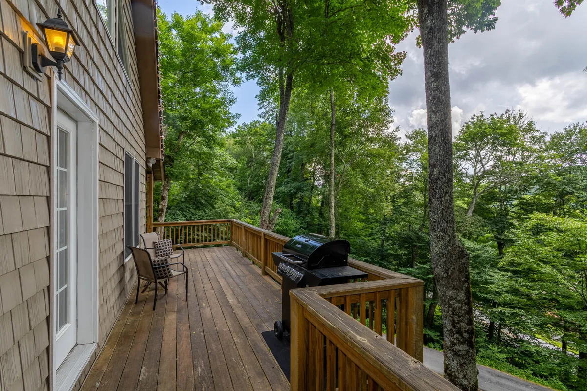 An inviting outdoor deck surrounded by mature trees, featuring a grill and a comfortable seating area. The deck offers a relaxing space to unwind, entertain guests, or simply soak in the natural mountain setting after a day of outdoor activities.