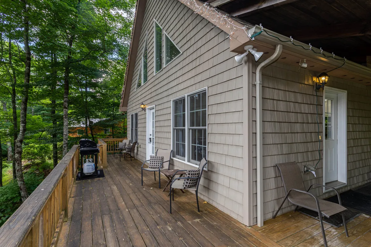 An exterior view of a wooden deck with outdoor seating and a grill, framed by trees. The space is perfect for outdoor dining, relaxation, and enjoying the fresh mountain air.