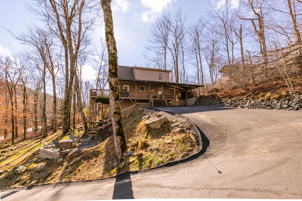 This image captures the exterior of the house surrounded by trees, with a clear focus on the freshly paved driveway leading up to the home. The tranquil mountain setting is evident, making it ideal for guests arriving for a winter getaway.