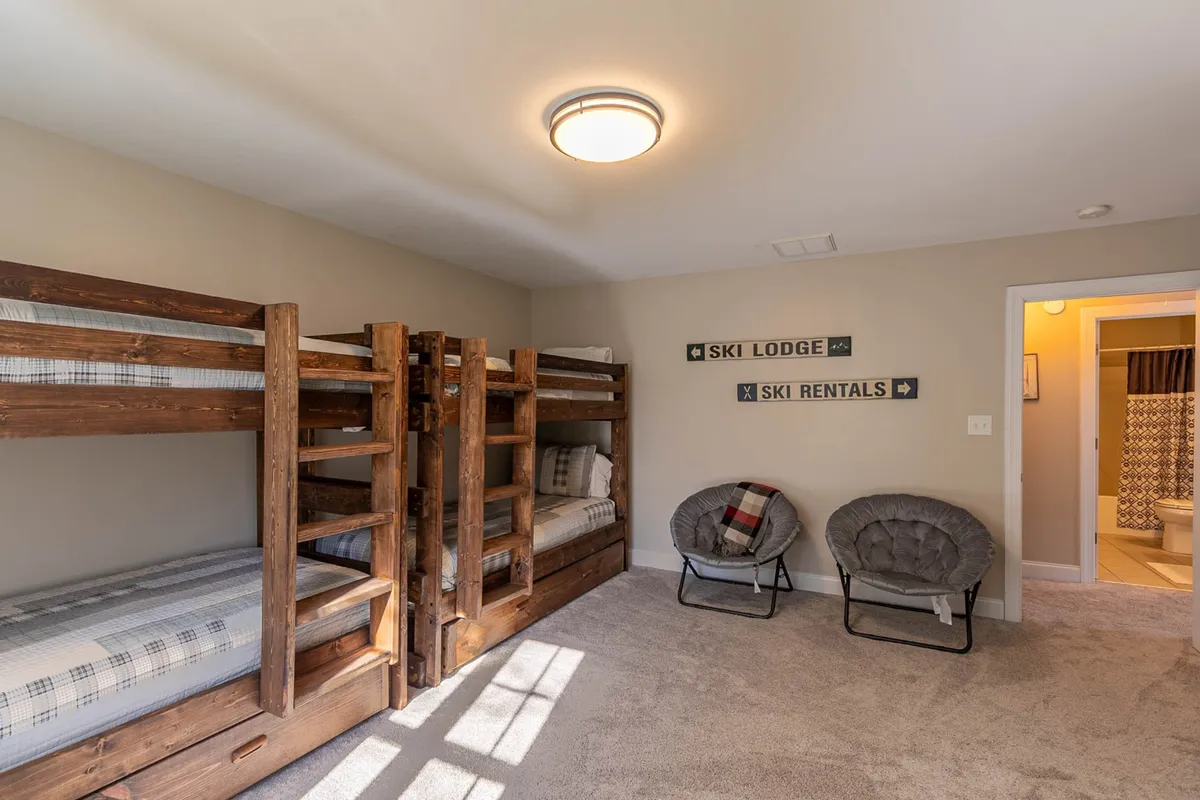 A second bunk room angle, with bunk beds, cozy chairs, and decorative wall signs that convey a sense of welcome and fun. The seating area hints at opportunities for conversation, relaxation, or games.