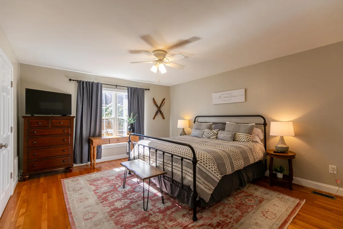 A tranquil bedroom scene featuring a king bed adorned with decorative pillows, a wooden dresser, a large window with curtains allowing in soft natural light, and tasteful wall art. The overall ambiance is serene and inviting, evoking a restful retreat perfect for unwinding after a day of adventure.