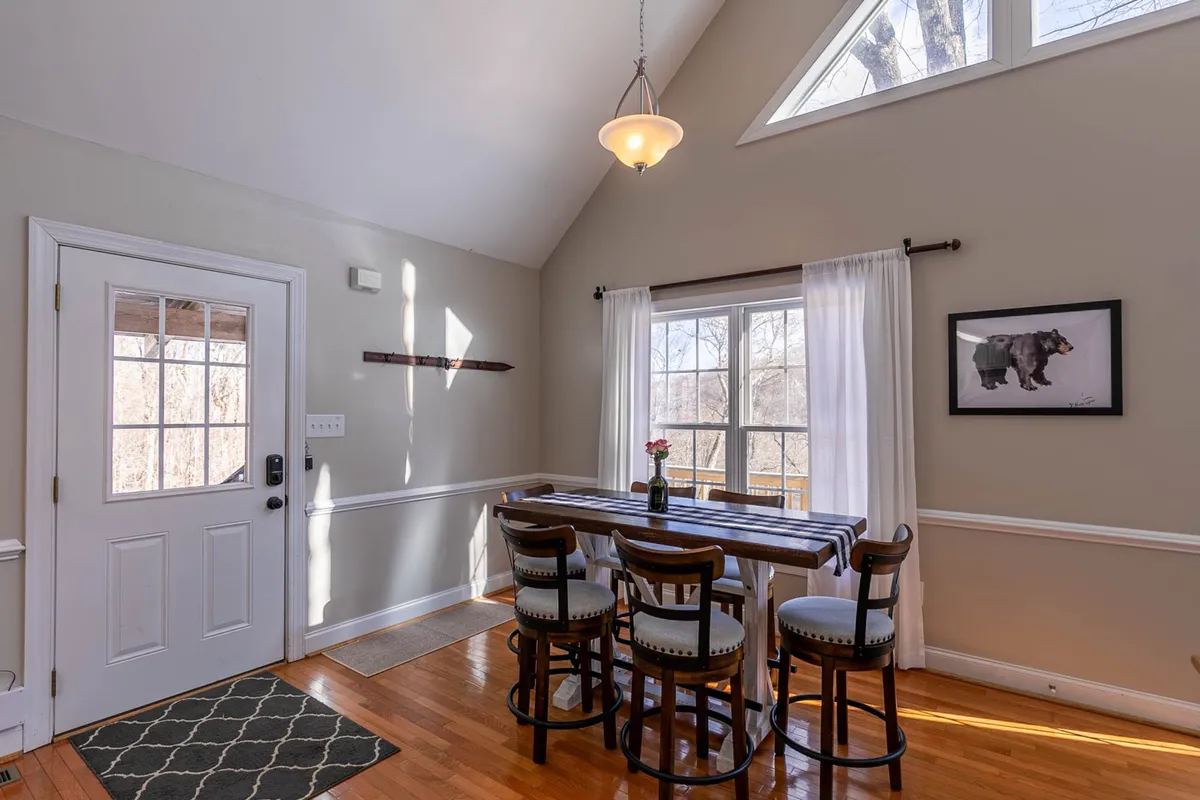 A bright dining area with a large table positioned by expansive windows, letting in morning light. The room features artwork and is set for casual or celebratory meals, evoking both everyday comfort and special gatherings.