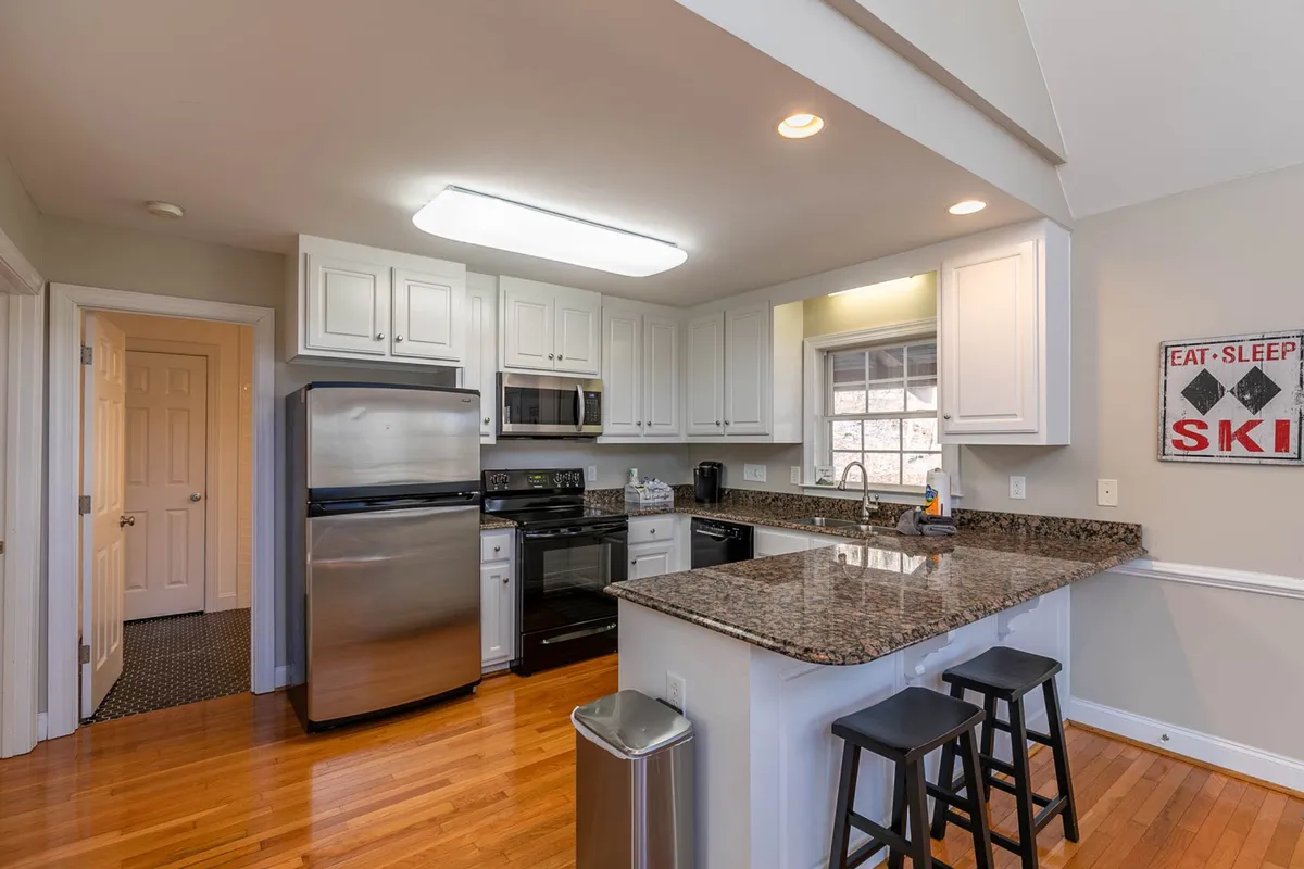 A kitchen scene featuring a granite countertop, stainless steel appliances, and wooden bar stools. The space is well-lit and inviting, suggesting a fully stocked, modern kitchen ready for meal preparation and gathering.